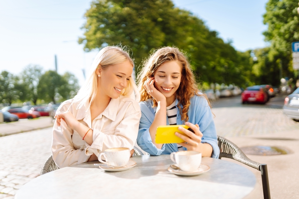 カフェでスマートフォンを見ながら楽しそうに話す女性達