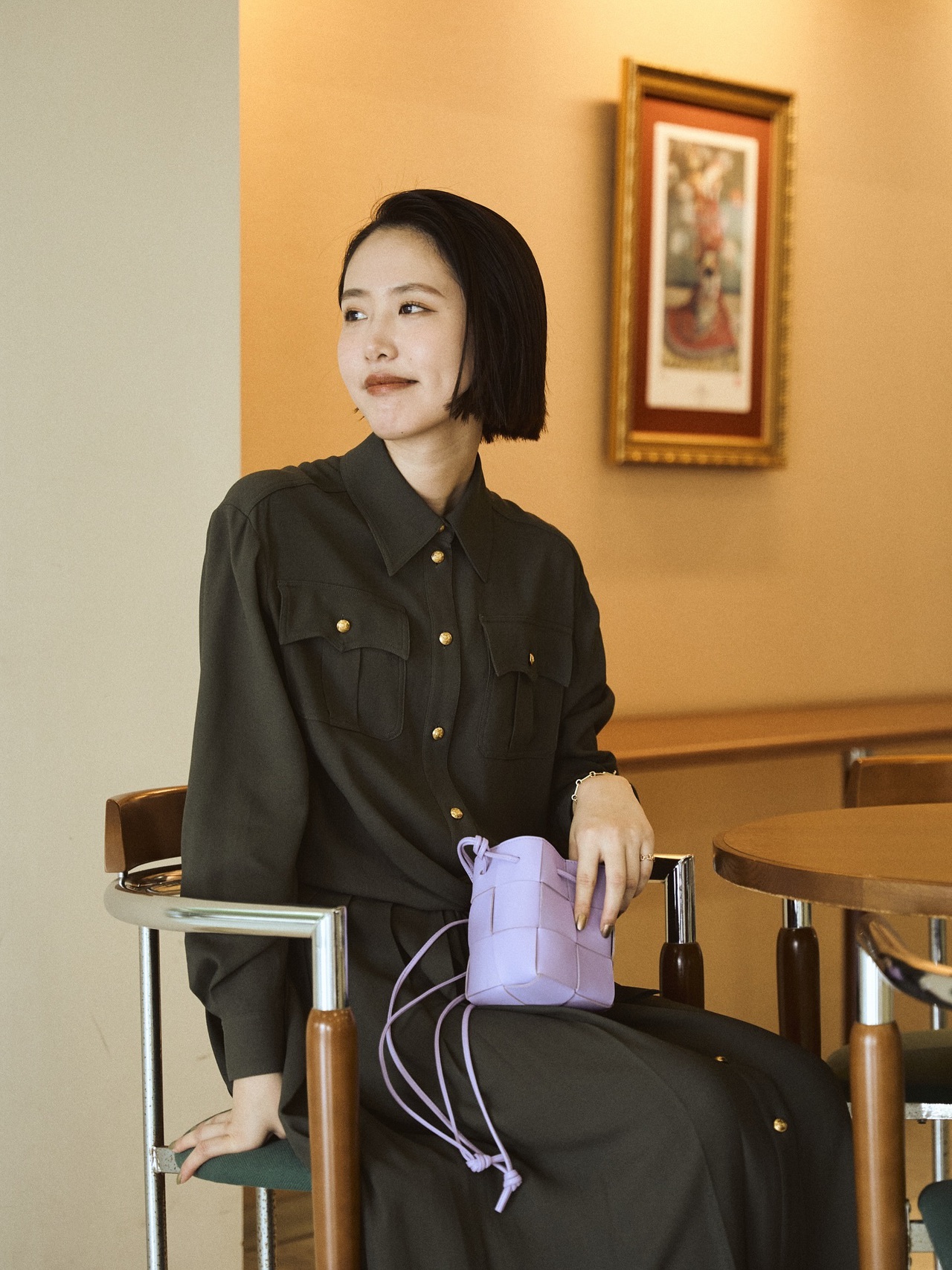 紫のミニバッグを膝に置き椅子に座る女性