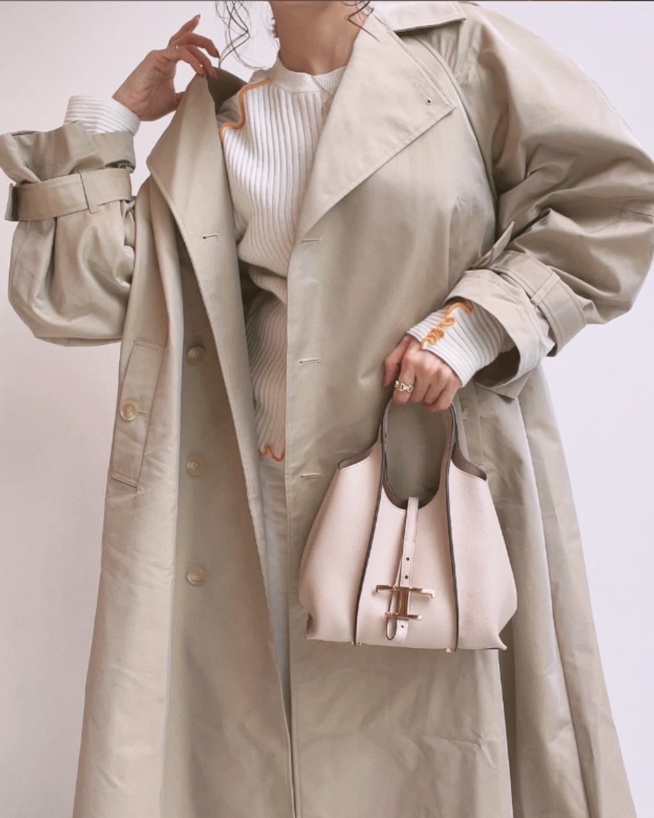 トッズのミニバッグを持ったベージュのコートを着た女性