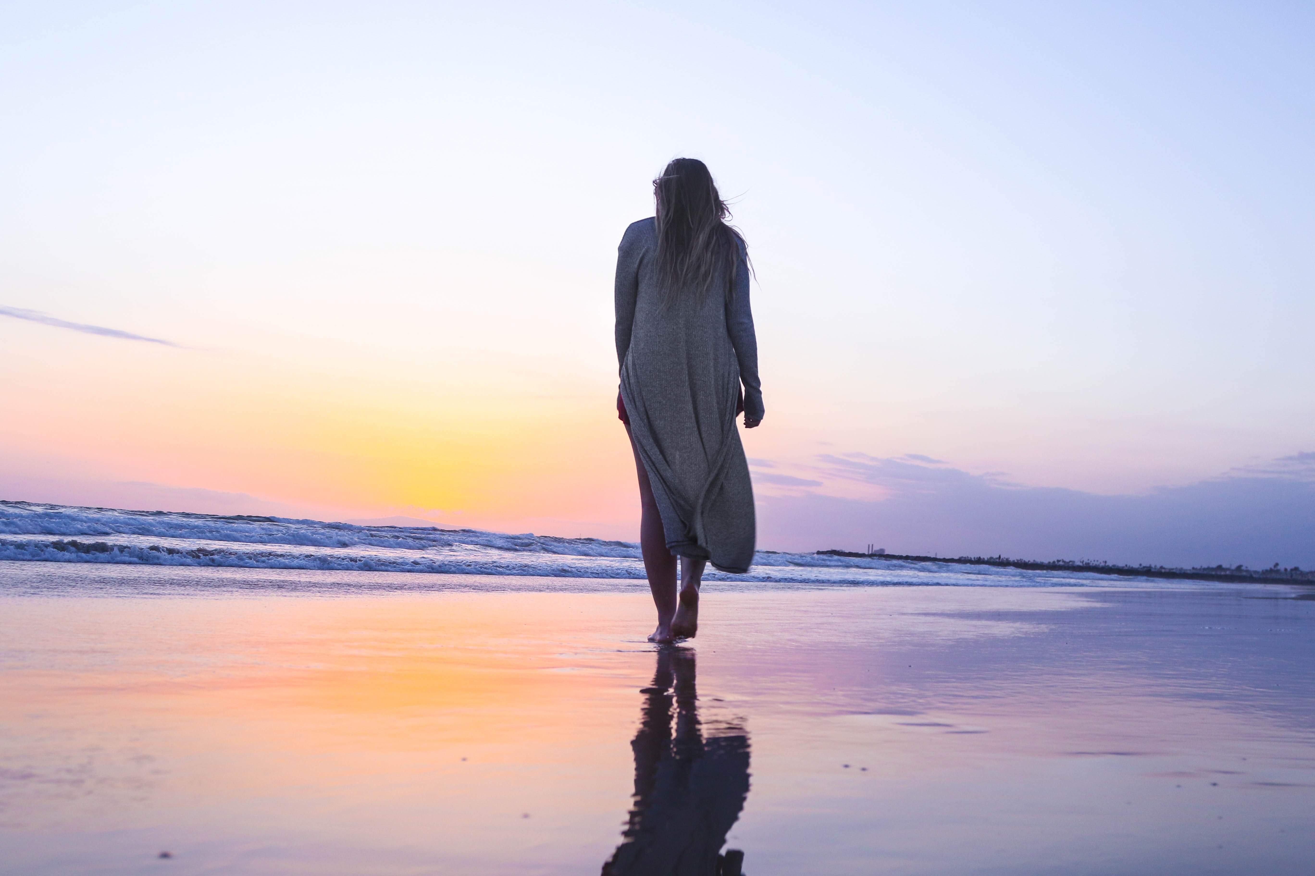 夕暮れ時に波打ち際にたつ女性