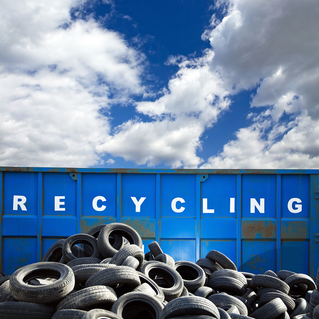 山積みの廃タイヤとブルー背景のRECYCLINGの文字
