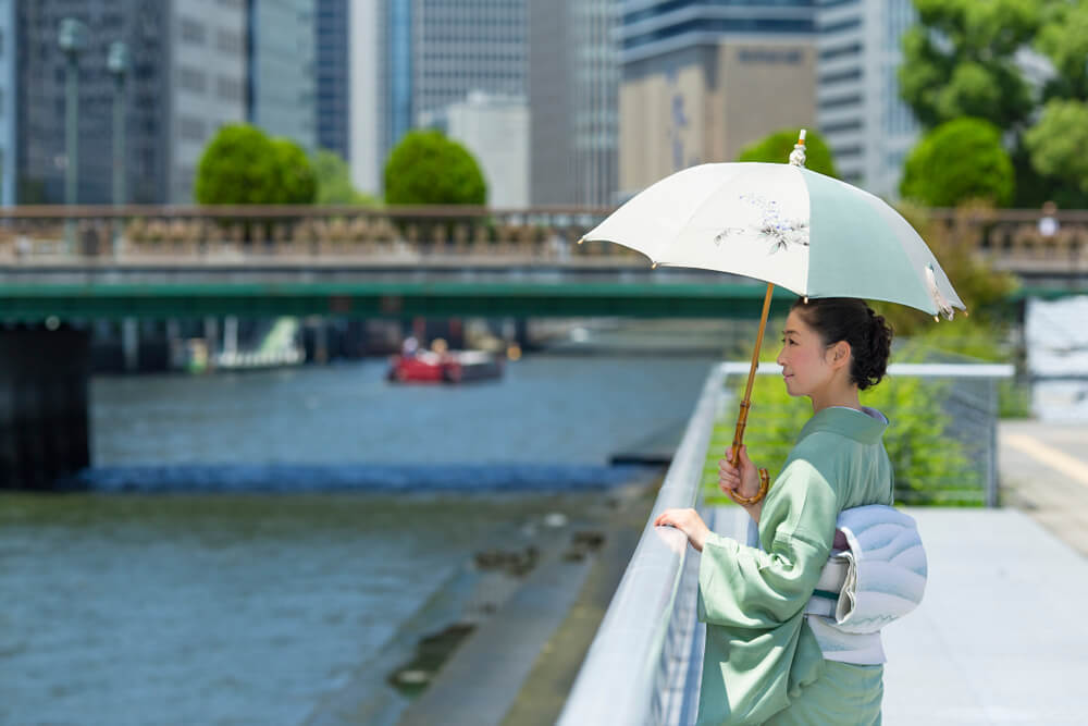 川辺で日傘をさして佇む着物女性